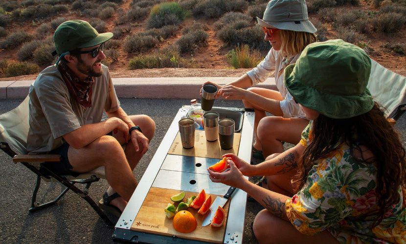 Three friends sit around an Entry IGT Table while preparing Michelada drinks using Snow Peak camping gear.