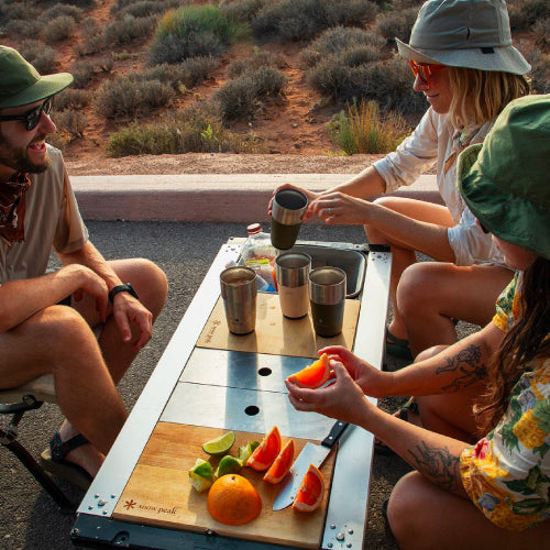 Three friends sit around an Entry IGT Table while preparing Michelada drinks using Snow Peak camping gear.