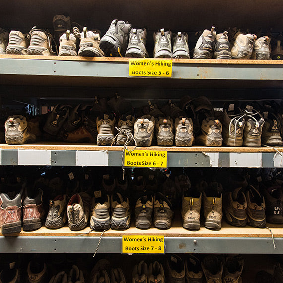 Shelves of gently worn hiking boots organized by size within an OEN gear library.