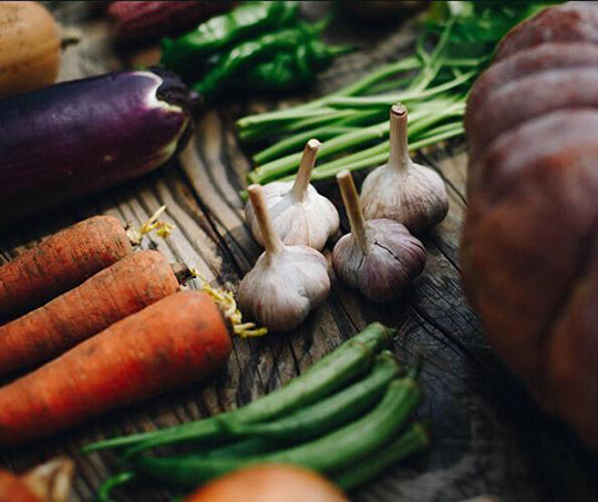 Fresh vegetables sit atop a wooden table.