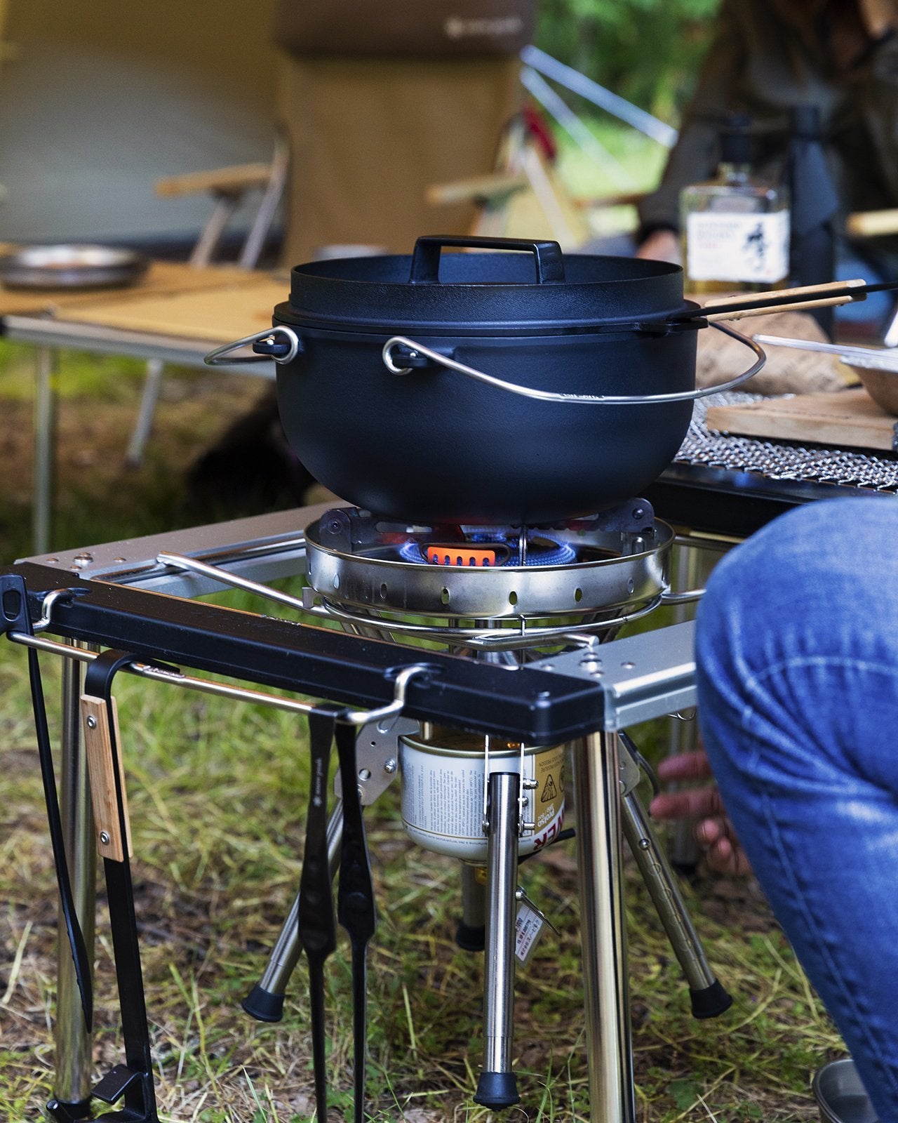 Camp cooking kit setup in use with a black pot on a portable stove in an outdoor setting.
