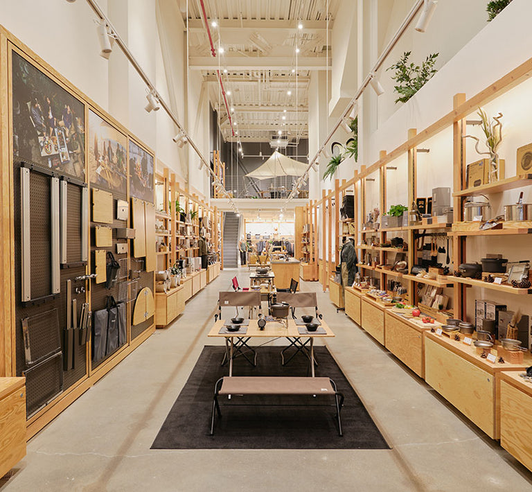 Interior of the Snow Peak Brooklyn store shows a long hallway lined with shelving on the right, displays on the left, and table displays in the center.